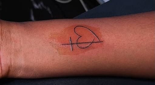 Fine-line tattoo of a heart crossed by a single line, placed on the inner forearm