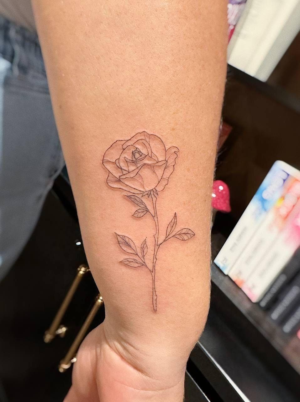 A custom fine-line rose tattoo on the forearm